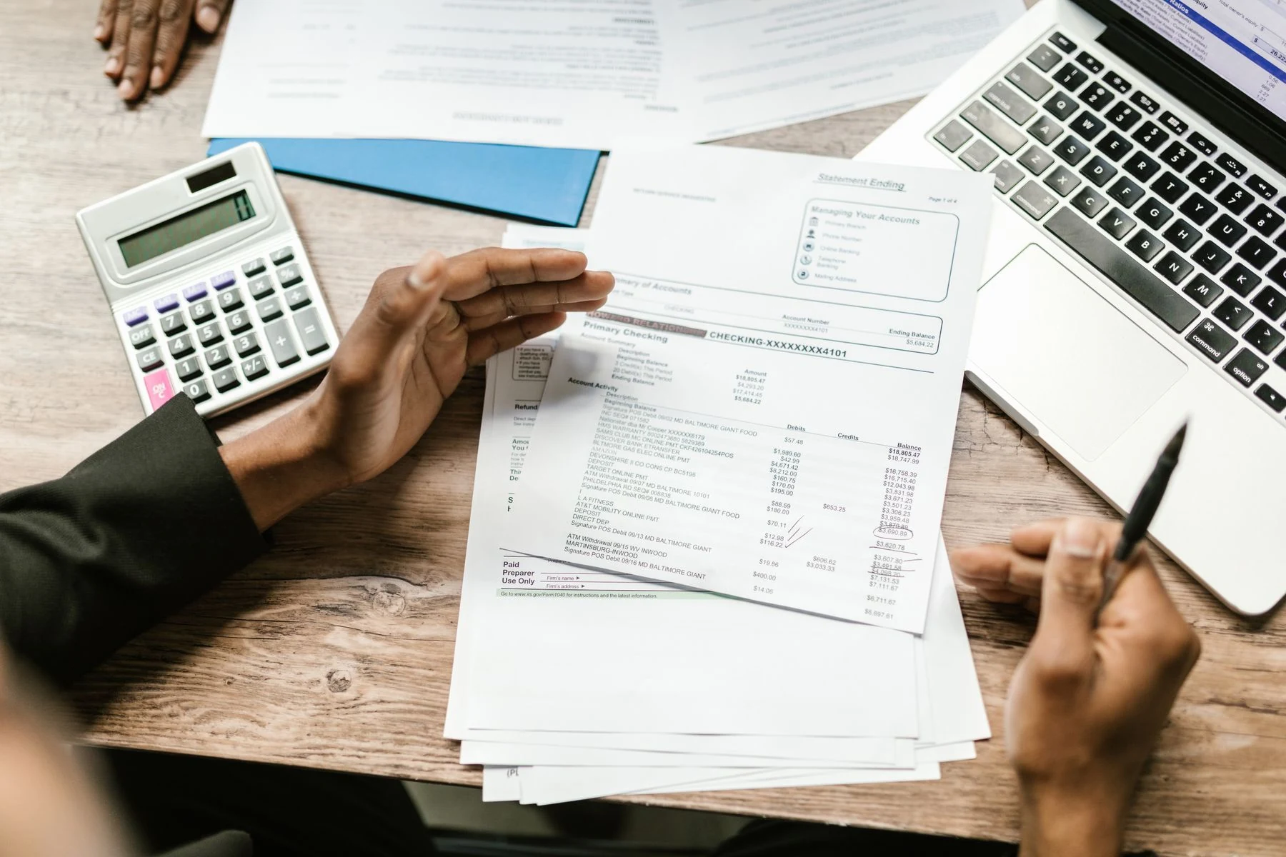 Hands checking a financial document beside a calculator and laptop